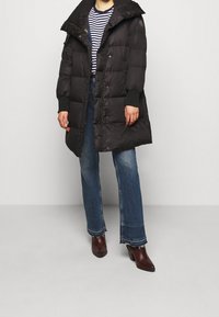 Svart pufferjacka med huva, med kviltad design och knappstängning. Matchad med en randig skjorta och jeans med utsvängda ben.