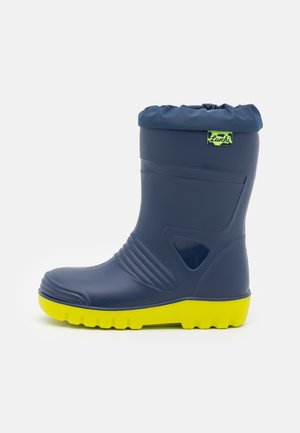 Navy rubber boot with a yellow sole, rounded toe, and ribbed design. Features a gathered top edge and a green logo patch. Waterproof material.