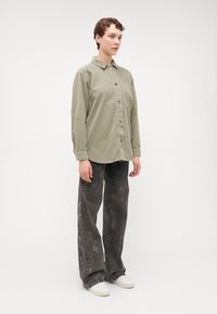 Chemise boutonnée en velours côtelé vert olive avec une poche poitrine, associée à un jean large à motif d'étoiles noirs et des baskets blanches.