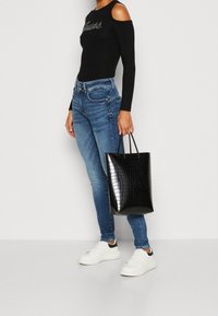 Zwarte nepleer tote bag met een krokodillenstructuur, plat ontwerp en korte handvatten. Gekocht bij blauwe skinny jeans en witte sneakers.