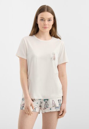 Jonge vrouw draagt een wit T-shirt met een kleine hondafbeelding en bijpassende witte short met kleurrijke hondenillustraties.