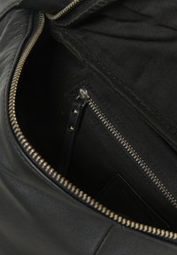 Interno di una borsa in pelle nera con tasca con zip, rivestimento in tessuto e etichetta in pelle, con zip in metallo visibile e dettagli di cucitura.
