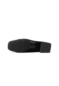 Scarpa nera slip-on con suola piatta, tacco in gomma testurizzata e tomaia liscia. Design minimalista, privo di decorazioni aggiuntive.