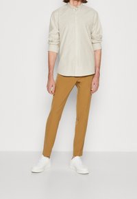 Lichtbeige button-up shirt met opgerolde mouwen, gecombineerd met mosterdkleurige slim-fitbroek en witte sneakers.