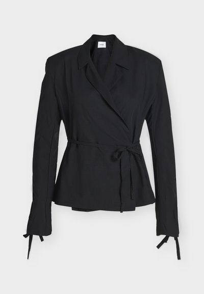 Blazer noir à manches longues avec col à revers et ceinture à la taille, avec liens aux poignets, présenté sur un fond blanc uni.