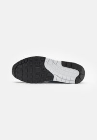 Semelle en caoutchouc noir avec un motif texturé et des accents gris. Présente un design plat avec une adhérence ferme et un talon renforcé pour plus de durabilité.