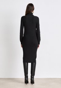 Svart ribbad trikåklänning med hög krage, figursydda lång ärmar och sidoklipp, kombinerad med knähöga svarta stövlar.