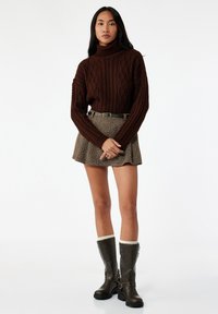 Maglione a collo alto marrone intrecciato, abbinato a una mini gonna a quadri infilata. Completato con stivali marroni alti fino al ginocchio con fibbie.