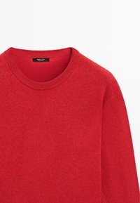 Maglione rosso a maglia con scollatura rotonda, superficie texturizzata e bordi del colletto a coste. Etichetta visibile all'altezza dello scollo.