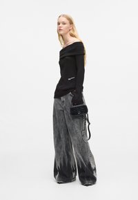 Melnā ribota blūze bez plecu siksnām ar garām piedurknēm, pārī ar platām, izbalējušām pelēkām biksēm ar tumšu apakšējo malu. Mazs melns maciņš ar siksnu.