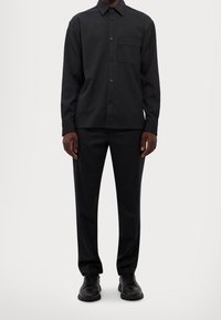 Zwarte, lange mouwen button-up shirt met een borstzak, gecombineerd met bijpassende zwarte broek en zwarte sneakers, met een gladde textuur en een tailored fit.
