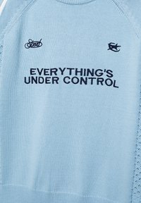 Világoskék kötött pulóver fekete "EVERYTHING'S UNDER CONTROL" felirattal és apró hímzett logókkal a felirat felett.