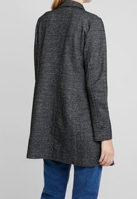 Giacca grigio scuro con motivo strutturato, maniche lunghe, collo a revers e dettagli con bottoni sui polsini, vista posteriore.