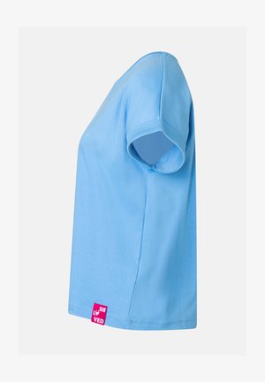 Hellblaues T-Shirt mit kurzen Ärmeln, seitlich gezeigt, mit einem kleinen pinkfarbenen Etikett nahe dem unteren Saum vor hellem einfarbigem Hintergrund.