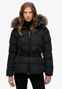 Giacca a piumino nera con vita cintrata, cappuccio staccabile foderato in pelliccia, design trapuntato e chiusura con zip frontale. Materiale morbido e isolante.