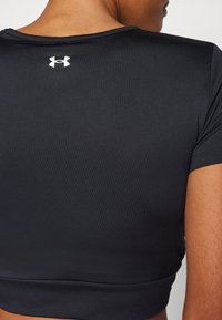 Top corto atletico nero realizzato in tessuto liscio e elasticizzato; presenta un collo rotondo e un piccolo logo bianco sul retro.