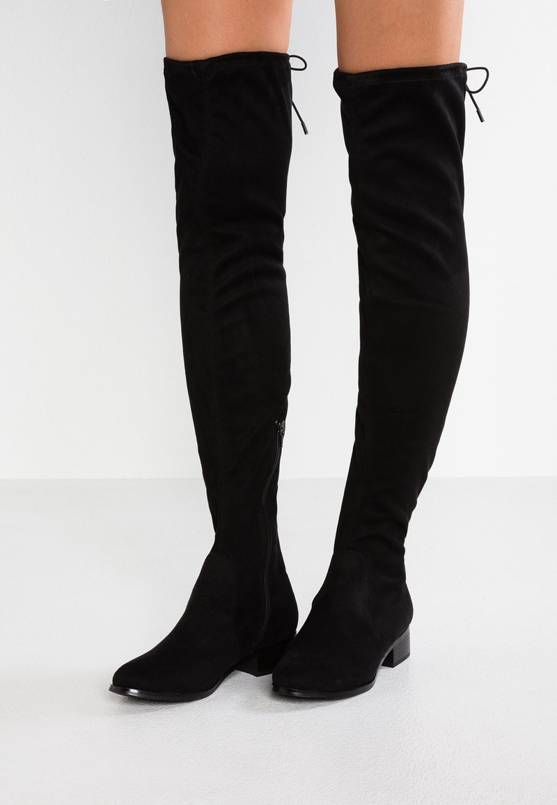 Bottes hautes en daim noir jusqu'au-dessus du genou avec une semelle plate, dotées d'une fermeture éclair latérale et d'un cordon de serrage ajustable en haut pour un maintien sécurisé.