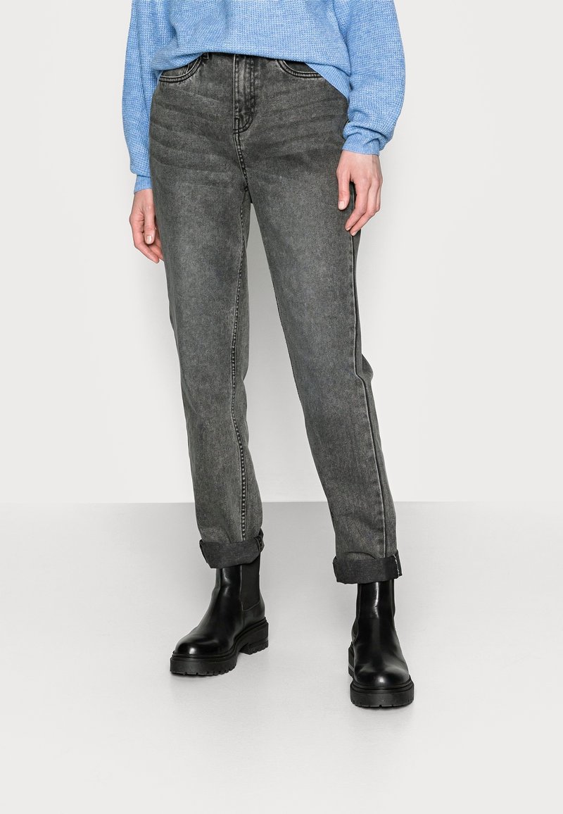 Vaqueros de denimb gris con un corte recto, costuras visibles y un dobladillo vuelto. Combinados con botas negras hasta el tobillo y un suéter azul claro.