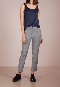 Débardeur en satin bleu marine associé à un pantalon à carreaux gris. Le pantalon présente une coupe ajustée, un devant plat et une longueur cheville. Des chaussures noires à lacets complètent la tenue.