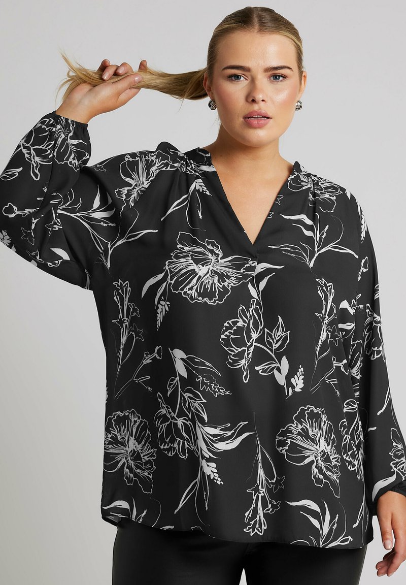 Blusa nera con motivo floreale bianco, scollo a V e maniche lunghe con polsini arricciati. Tessuto liscio, vestibilità ampia e caduta morbida.