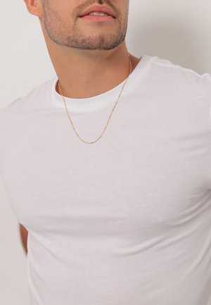 Tricou alb din bumbac cu guler rotund. Are o croială slim și o textură uniformă. Se poate observa o brățară subțire din aur.