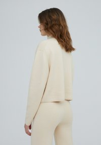 Lichtbeige cropped sweater van zachte brei, met een ontspannen pasvorm, verlaagde schouders en geribde manchetten, gecombineerd met bijpassende leggings.