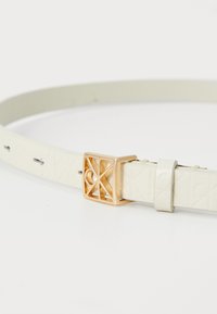 Weißer Kunstledergürtel mit einer polierten goldenen rechteckigen Schnalle mit Ausschnittdesign und geprägten Details entlang des Riemens.