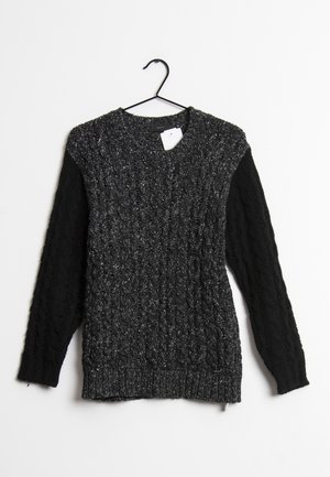 Pull en maille torsadée gris foncé avec manches noires suspendu à un cintre noir sur fond blanc.