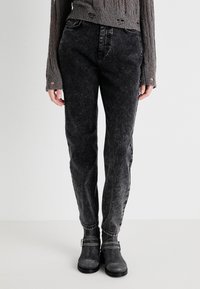 Zwarte gewassen denim jeans met een ontspannen pasvorm, voorzien van subtiele vervaging, vijf zakken en een rechte pijp. Ggedragen met grijze enkellaarsjes.