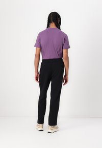 Camiseta corta de manga corta morada combinada con pantalones negros y zapatillas beige, con un corte relajado y cinturilla elástica. Diseño simple, sin patrones.