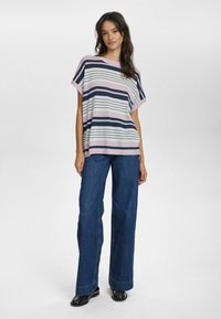 Svītrainā adītā krekls rozā, tumši zils un balts; ar platām piedurknēm un brīvu piegriezumu. Apģērbs saskaņots ar plašiem ziliem džinsiem un melniem apaviem.