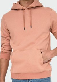 Rosa huvtröja i mjukt tyg, med en känguruficka, dragsko med svarta ändar och ribbade ärmmuddar.