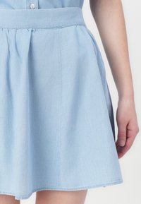Light blue denim skirt with a flared design, elastic waistband, and side pleats, featuring a smooth texture and a hem that falls above the knee.