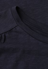 Gros plan sur un tissu bleu marine foncé présentant un col rond avec bordure côtelée et détails subtils de couture.