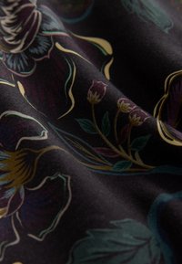 Tissu noir avec un motif floral aux détails vibrants en vert, violet et or ; texture lisse avec des dessins complexes et des formes fluides.
