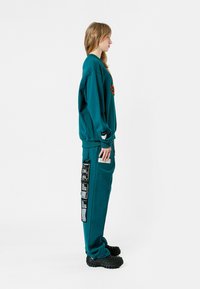 Sudadera azul pálido oversized con detalles bordados, combinada con joggers a juego que cuentan con bolsillos laterales y acentos de parches. Calzado negro grueso.