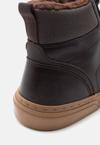 Fekete bőr bokacsizma textúrált mintával, barna műszőrme béleléssel és világosbarna gumi talppal. Kontrasztos varrással és húzófüllel rendelkezik.