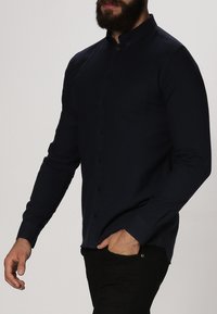 Donkerblauwe lange mouwen overhemd met knopen en een kraag, voorzien van een borstzak en een soepele textuur, gedragen met donkere broek.