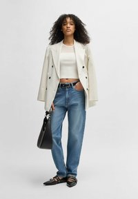 Dubbla bröstet randig blazer, vit kort topp, ljusblå jeans, svart handväska, svarta spetsiga flats med remmar och nitar.