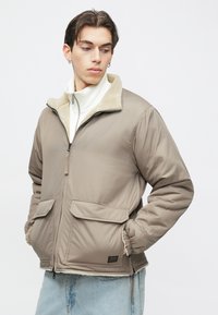 Dunjakke i taupe med fleeceforet krave, lynlås foran og to forlommer; tekstureret stof med elastiske manchetter.