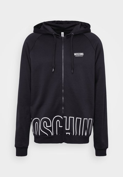 Black zip-up hoodie with a soft texture, featuring a white "MOSCHINO" logo at the bottom and on the left chest. Ribbed cuffs and hem.