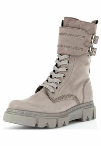 Beige suede ankle boot with front lacing, adjustable strap and buckles, chunky rubber sole, and stitching details.