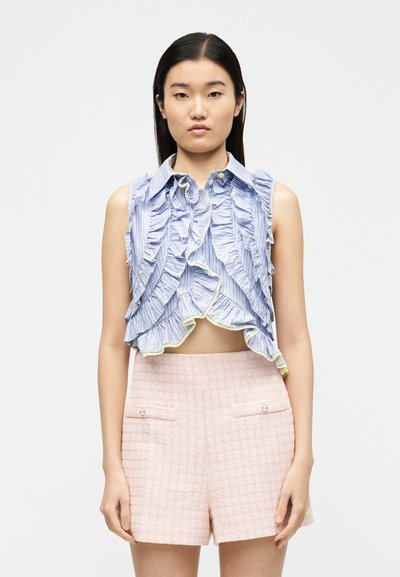 Γυναίκα με αμάνικο crop top σε μπλε και λευκές ρίγες με βολάν και ψηλόμεσο ροζ σόρτς με υφή και τσέπες με κουμπιά από πέρλες.