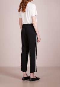 Svarta träningsbyxor med vita sidostråk, med en avslappnad passform och elastisk midja. Matchas med en löst sittande vit t-shirt.