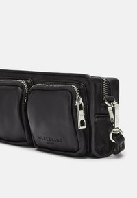 Bolso de cuero negro tipo bandolera con dos bolsillos con cremallera, herrajes plateados y una textura suave, con el nombre de la marca grabado en la parte delantera.
