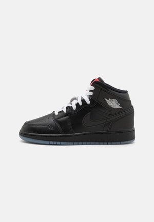 Sneaker mid-top din piele neagră, cu șireturi albe, talpă gri și accente roșii; prezintă vârf perforat și logo-ul Air Jordan pe lateral.