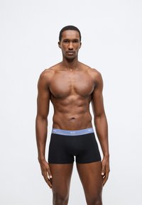 Boxeri negri cu talie elastică albastră inscripționată cu „BOSS”. Materialul pare neted, cu un design modern și ajustat.