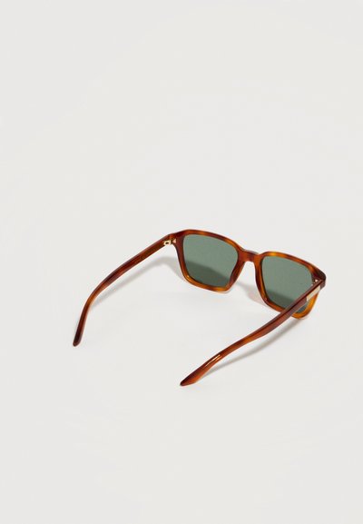 Lunettes de soleil écaille de tortue marron avec verres verts rectangulaires posées ouvertes sur une surface claire.