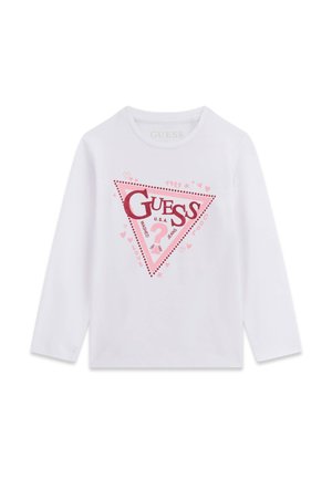 Chemise blanche à manches longues avec un logo triangulaire rose et rouge affichant le mot "GUESS", un point d’interrogation et de petits motifs en forme de cœur et d’étoile.