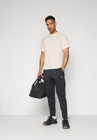 Camiseta de color beige claro, pantalones de chándal negros con el logo de Nike, bolsa deportiva negra. El conjunto presenta un ajuste casual y un diseño elegante, adecuado para ropa atlética.